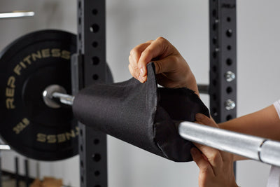 Woman wrapping Fitness Barbell Shoulder Pad on barbell, soft, durable squat and hip thrust pad with Velcro closure for easy attachment; protects shoulders, neck, and hips during lifts; made from nitrile rubber and Oxford cloth; 17” long, 4” diameter with white REP Fitness logo stitching for comfort and stylefrom Rep Fitness UK | Shop Premium Gym Equipment for Home & Commercial Use, Best Online Gym Equipment UK